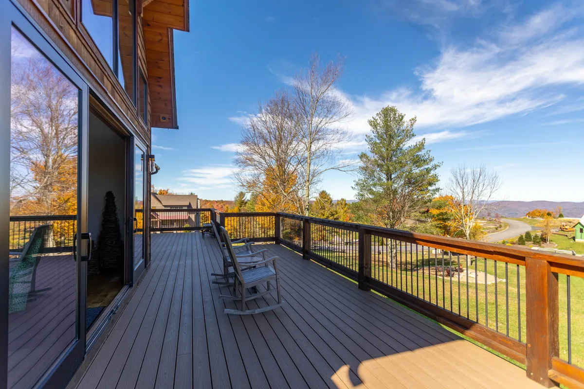 A serene deck is pictured, featuring rocking chairs that look out over a breathtaking mountain view. The scene suggests peaceful mornings with coffee, relaxing afternoons soaking in nature, or evenings spent watching sunsets.