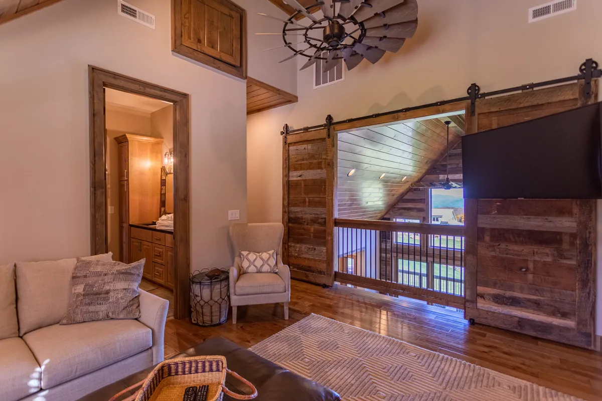 A comfortable seating area anchored by a rustic wooden sliding door and large ceiling fan, offering a cozy spot for reading, watching TV, or enjoying a quiet cup of coffee. The space feels inviting and is perfect for shared moments with family or friends.