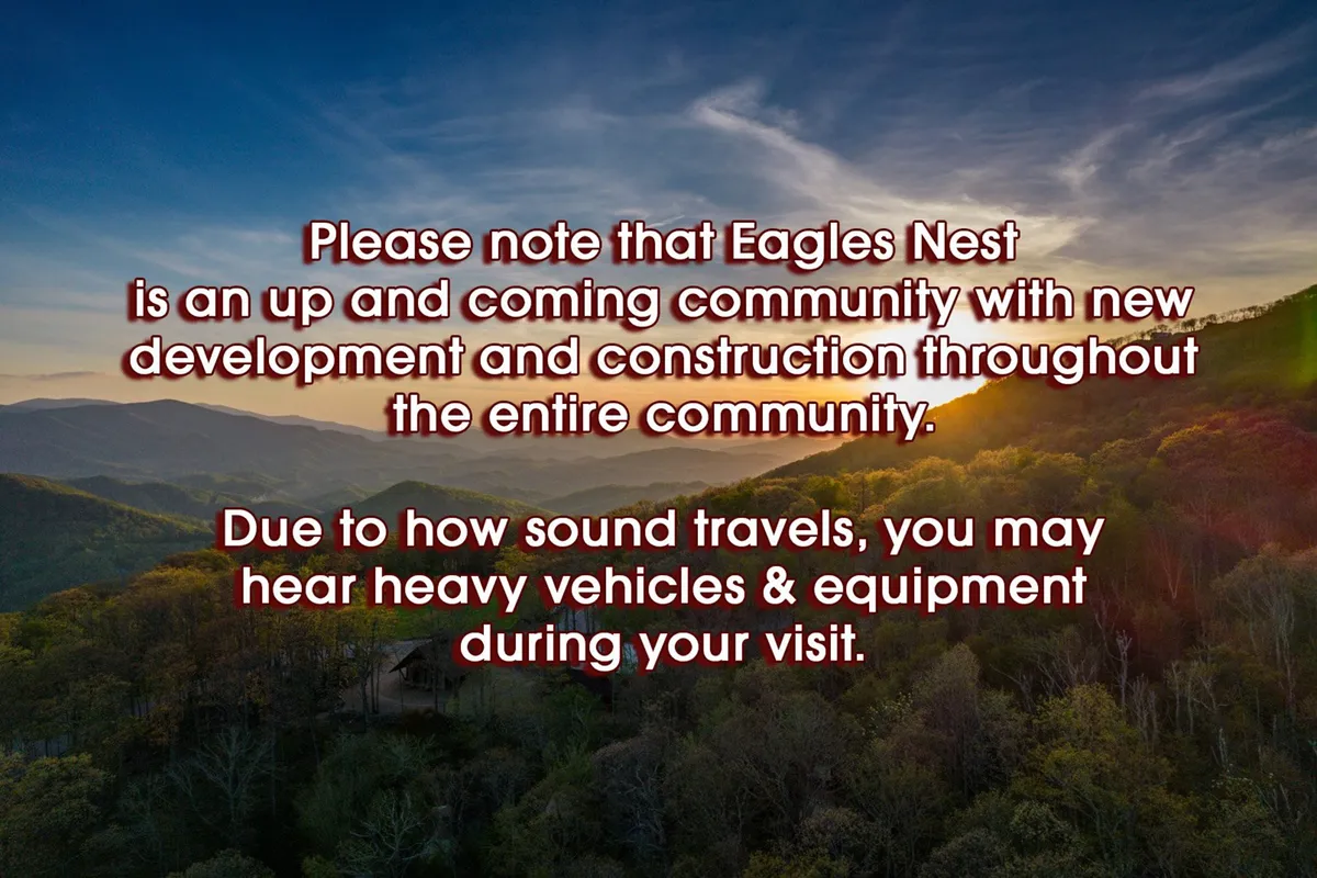 This image captures a sweeping mountainous landscape beneath a colorful sunset sky, with a subtle construction notice visible in the distance. The view balances natural beauty with cues about ongoing development within the community.