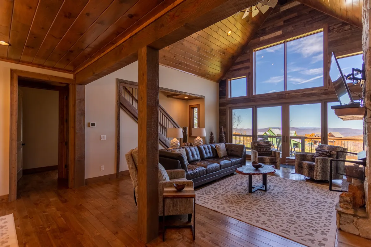 A spacious living area with large windows offering scenic mountain views, a comfortable leather sofa, rustic wooden beams overhead, and a stylish coffee table. The room invites relaxation and social connection, with ample light streaming in and decorative accessories that add warmth.