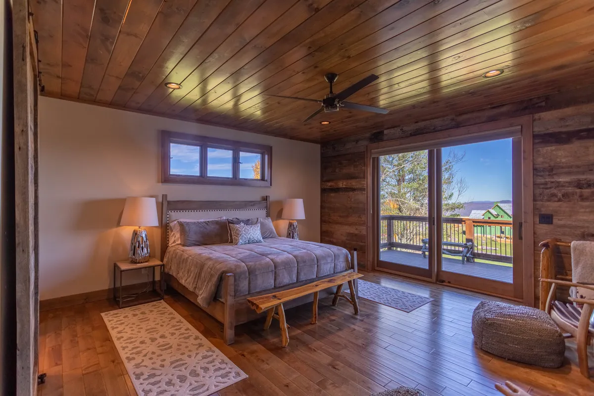 A serene king bedroom featuring a plush bed set against large windows that invite natural light and offer a calming view. The wooden ceiling adds warmth, while the tranquil decor creates a restful atmosphere—perfect for parental or couple retreats.
