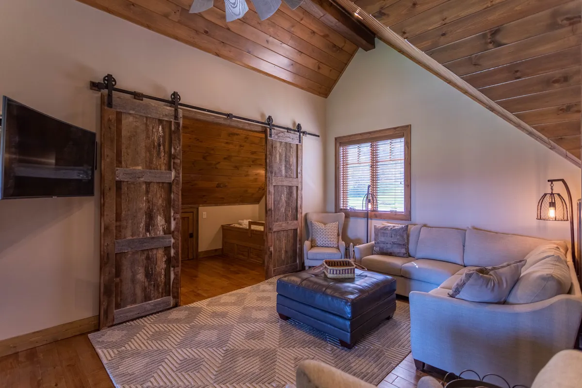 A lofted entertainment space featuring a comfortable sectional sofa, textured rug, and sliding barn doors under a wooden ceiling. The area feels inviting and flexible—ideal for family relaxation or imaginative play.